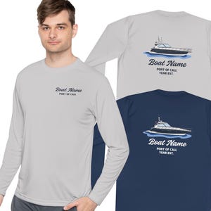 Op de afbeelding: Shirts met lange mouwen in lichtgrijs en marineblauw, met een bootafbeelding op de rug. De shirts tonen de tekst "Boat Name, Port of Call, Year Est." op de rug en voorkant. De shirts worden op een persoon getoond.