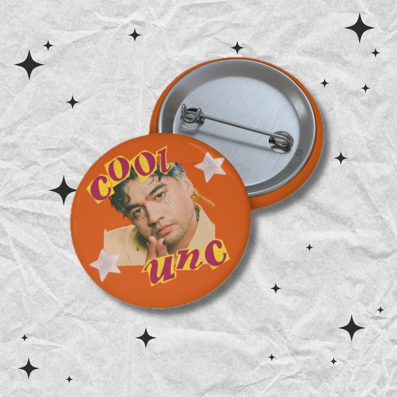 May include: Orange button with a portrait of a person with blue and yellow hair, the word "COOL" in pink, and the word "unc" in yellow. Two white star shapes are also on the button. A second button is visible.