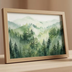 May include: A framed watercolor painting of a misty forest scene. The artwork features a landscape of green trees and mountains, with a light brown wooden frame. A small succulent in a white pot sits on a wooden surface.