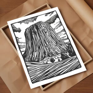 May include: Black and white woodcut print of a tall, thin rock formation with a cloudy sky in the background. The rock formation is called "Devils Tower" and is located in Wyoming, USA.