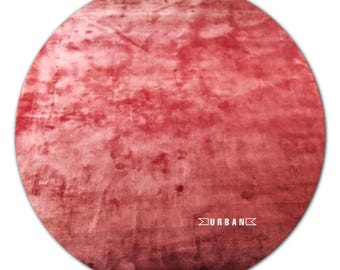 May include: A round, red rug with a gradient effect, fading to a lighter shade of red at the edges. The rug has a soft, fuzzy texture and the word "URBAN" is printed in white in the lower right corner.