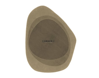 Könnte beinhalten: Eine braune abstrakte Form mit einem geschichteten Design. Die Form hat eine glatte, strukturierte Oberfläche und ein subtiles, verblasstes Aussehen. Das Wort "URBAN" ist in schwarzer Schrift in der Mitte der Form gedruckt.