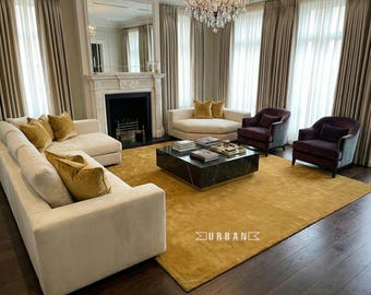 May include: A luxurious living room with a mustard yellow rug, cream-colored sofas, and dark purple armchairs. A black marble coffee table sits in the center, and the room is illuminated by a chandelier and natural light.