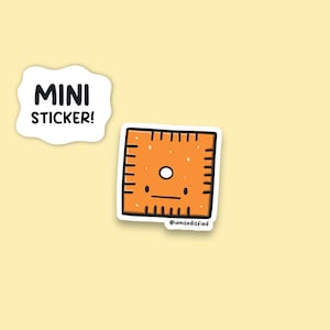 May include: A small orange sticker with a cartoon square shape with a white circle and a black line for a mouth. The sticker says "MINI STICKER!" and "@iamsatisfied" in black text.