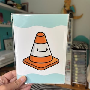 May include: A print featuring a cartoon traffic cone with a minimalist face. The cone is orange and white, set against a light blue wavy background. The print is in a clear plastic sleeve.