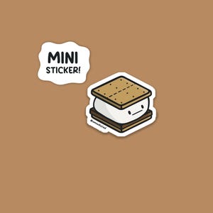 May include: A mini sticker featuring a cartoon s'more with a smiling face. The s'more is made of graham crackers, marshmallow, and chocolate. A separate white sticker with the words "MINI STICKER!" is also present.