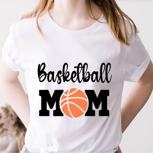 May include: White t-shirt with black text that reads "Basketball Mom" and a black and orange basketball graphic.