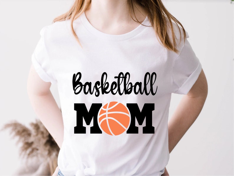 May include: White t-shirt with black text that reads "Basketball Mom" and a black and orange basketball graphic.