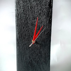 Puede incluir: Un reloj negro con agujas rojas sobre un fondo negro texturizado.