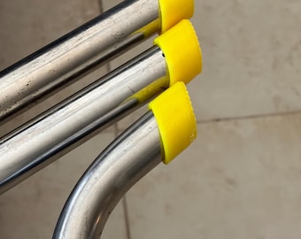 Puede incluir: Primer plano de tres tubos metálicos brillantes y curvados con tapas protectoras amarillas brillantes. Los tubos están dispuestos en un patrón ligeramente superpuesto, con las tapas amarillas en la parte superior. El fondo es una superficie neutra de color claro.