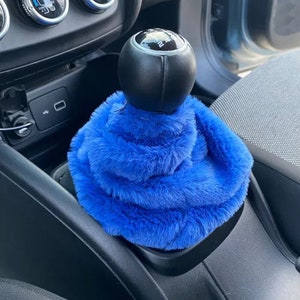 May include: Blue faux fur gear shift cover for a car. The cover is soft and fluffy and fits over the gear shift knob.