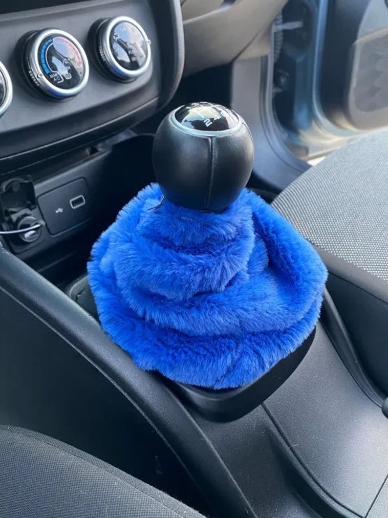 May include: Blue faux fur gear shift cover for a car. The cover is soft and fluffy and fits over the gear shift knob.