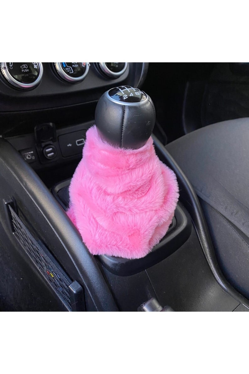 May include: Pink faux fur gear shift cover for a car. The cover is soft and plush and fits over a standard gear shift knob.