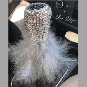 Könnte beinhalten: Ein silberner Schaltknauf, der mit Strasssteinen besetzt ist, mit einem grauen Federboa, der an der Unterseite befestigt ist. Der Text "Yaxo Design" ist im Hintergrund sichtbar.