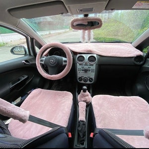 May include: Pink fuzzy car seat covers, steering wheel cover, and dashboard cover. The car has a black interior and a black steering wheel.