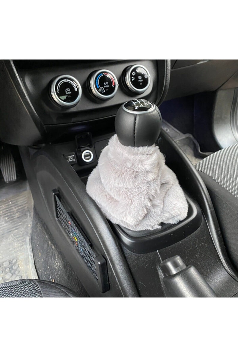 May include: A grey faux fur gear shift cover with a black leather gear shift knob. The gear shift knob has a silver gear shift pattern with the numbers 1, 2, 4, 5, and 6.