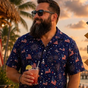 May include: A short-sleeved button-down shirt featuring a navy blue background with a repeating pattern of American flags and fireworks, paired with solid red shorts and dark flip-flops. The shirt has a classic collar and white buttons.
