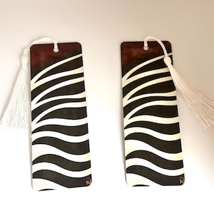 May include: Two rectangular bookmarks with a zebra stripe design. The top portion is a dark brown gradient, transitioning to white zebra stripes on a black background. Each bookmark has a white tassel attached at the top.