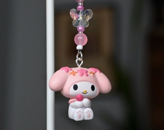 May include: A pink and white charm with a cartoon character wearing a pink flower crown and holding a pink heart. The charm is attached to a silver chain with pink and white beads and crystal butterfly charms.