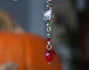 May include: A silver key chain with a red strawberry charm, green and red beads, and a clear crystal butterfly charm.