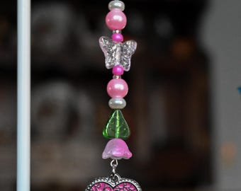 May include: A beaded keychain with a silver ring. The keychain features pink beads, a clear butterfly charm, a green leaf, a pink flower, and a heart-shaped charm with a white cat design and pink accents.