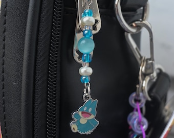 May include: A silver-toned metal zipper pull charm featuring a blue and white cartoon creature pendant. The charm is strung with alternating translucent blue beads, small white pearls, and a larger light blue cat-eye bead on a silver chain.