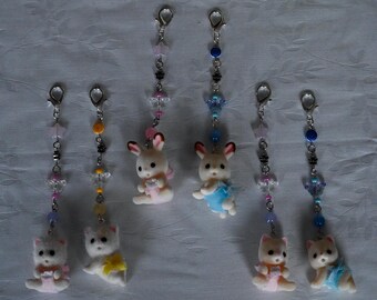May include: Six hanging charms featuring miniature flocked animal figures, including rabbits and cats. Each charm is attached to a silver-tone lobster clasp and decorated with colorful beads, star-shaped accents, and small metal spacers on a chain.