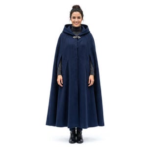 May include: A floor-length navy blue wool cape featuring a hood, a high collar, and a decorative silver-toned metal clasp at the neckline. The garment has a structured silhouette with arm slits on the sides and a smooth, solid-colored fabric finish.