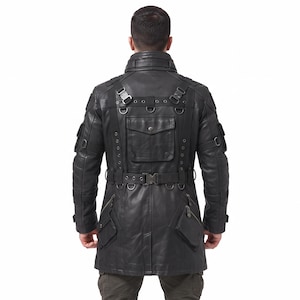May include: A black leather jacket featuring a high collar, multiple utility pockets, and a waist belt with a buckle. The back design includes integrated straps, metal D-rings, and eyelet details, creating a structured, tactical appearance.