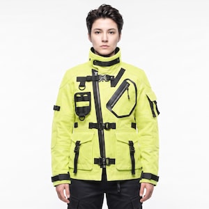 May include: A neon yellow utility jacket featuring a high collar, an asymmetrical black zipper closure, and multiple black buckled straps. The jacket includes several external pockets, black webbing loops, and adjustable cuffs on the long sleeves.