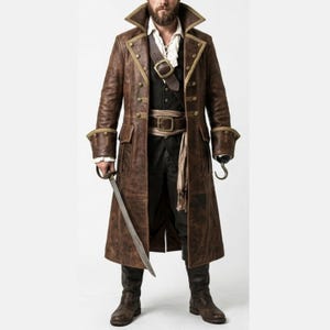 Puede incluir: Un abrigo de pirata de cuero marrón con ribetes dorados, botones de doble botonadura y un cuello ancho. El abrigo presenta un cinturón, una camisa blanca, pantalones negros y botas. También se ven una espada y un garfio.