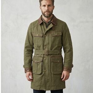 May include: An olive green field jacket featuring a brown leather collar and matching leather cuffs. The jacket includes four front flap pockets with snap closures, a central button placket, and a matching fabric belt with a rectangular buckle.