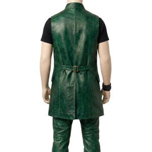 Puede incluir: Un chaleco largo de cuero verde con cuello alto, una costura vertical en el centro de la espalda y una correa horizontal en la cintura con una hebilla met&aacute;lica rectangular. La prenda tiene dos bolsillos laterales y un dobladillo con abertura, sobre una camiseta negra.