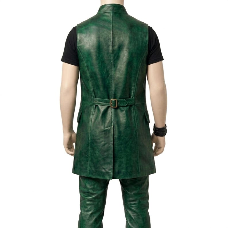 Puede incluir: Un chaleco largo de cuero verde con cuello alto, una costura vertical en el centro de la espalda y una correa horizontal en la cintura con una hebilla met&aacute;lica rectangular. La prenda tiene dos bolsillos laterales y un dobladillo con abertura, sobre una camiseta negra.