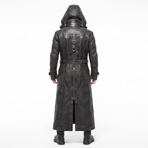 May include: A black long coat featuring a hood, a high collar with buckle straps, and a harness-style back detail. The garment includes a vertical back zipper, long sleeves with buckled cuffs, and a structured design with visible seam lines.