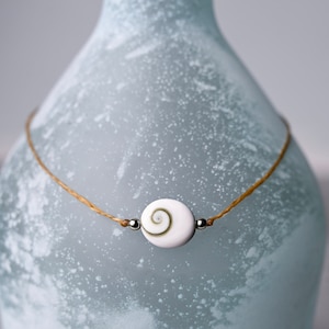 May include: A simple necklace with a white shell pendant and silver beads on a brown cord.