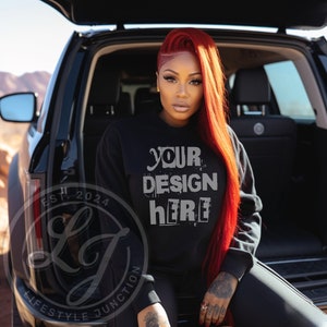 May include: A black sweatshirt with the text "YOUR DESIGN HERE" in white. The sweatshirt is being worn by a person with long red hair. The person is sitting in the back of a black car.