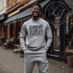 May include: A grey sweatshirt with the text "FORGIVE & FORGET" printed in black. The sweatshirt is being worn by a person standing in front of a brick building.
