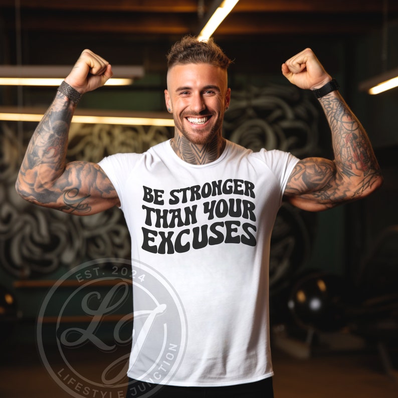 Op de afbeelding: Wit T-shirt met zwarte tekst die "BE STRONGER THAN YOUR EXCUSES" luidt in een retro lettertype. De tekst is gecentreerd op het shirt.