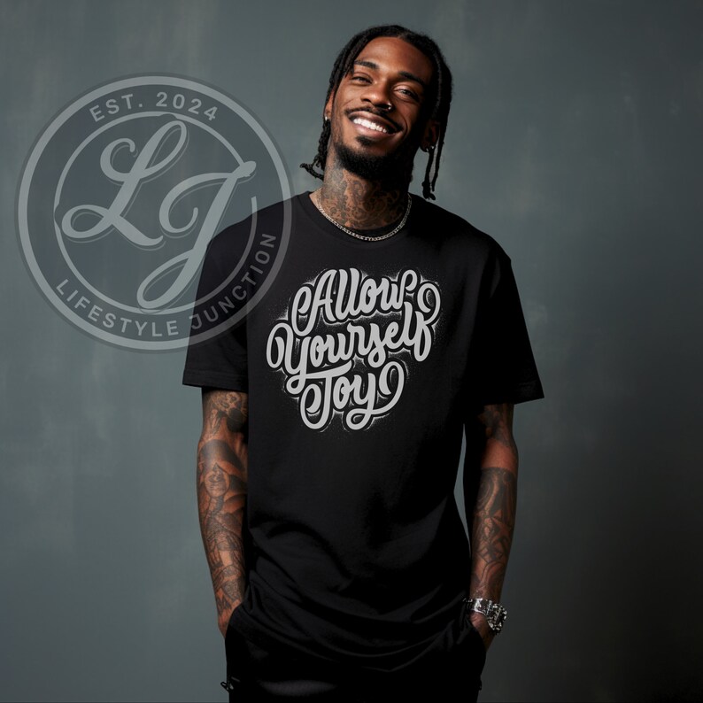 Puede incluir: Una camiseta negra con un gr&aacute;fico blanco que dice "Allow Yourself Joy" en una fuente estilizada. La camiseta la lleva puesta una persona con tatuajes en los brazos.