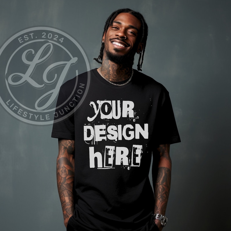 Puede incluir: Una camiseta negra con el texto "YOUR DESIGN HERE" en blanco, impreso en un estilo desgastado. La camiseta est&aacute; siendo modelada por una persona con tatuajes.