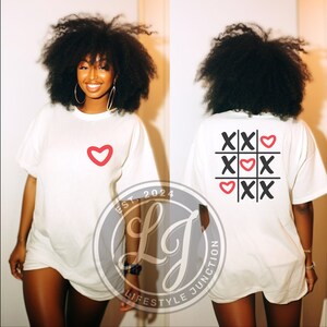Peut inclure: T-shirt blanc surdimensionn&eacute; avec un c&oelig;ur rouge sur le devant et un c&oelig;ur rouge et des X noirs en forme de tic-tac-toe au dos. Le t-shirt porte le texte "EST. 2024 LJ LIFESTYLE JUNCTION" en bas &agrave; gauche.