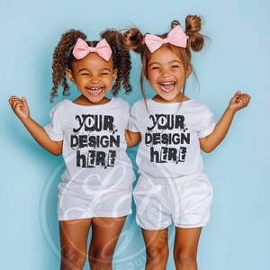 Puede incluir: Dos ni&ntilde;as peque&ntilde;as con camisetas blancas con el texto "YOUR DESIGN HERE" impreso en ellas. Est&aacute;n sonriendo y mirando a la c&aacute;mara. Las ni&ntilde;as llevan lazos rosas en el pelo.