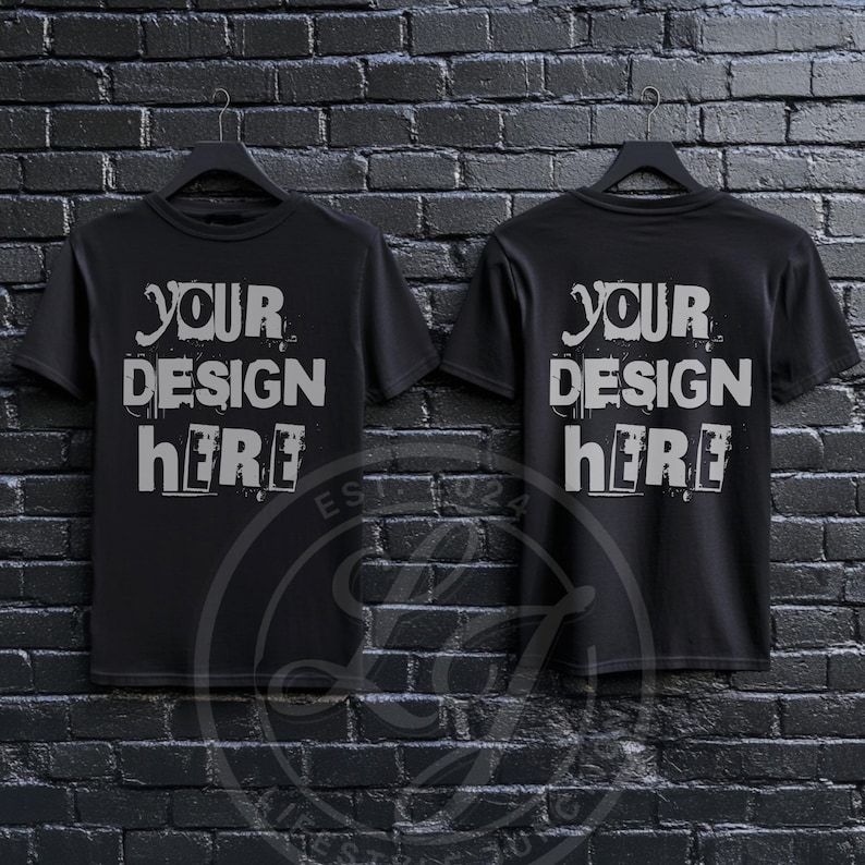 May include: Two black t-shirts with short sleeves hanging on hangers against a black brick wall. The front of each shirt says "YOUR DESIGN HERE" in a distressed white font.