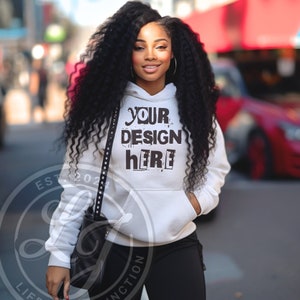 May include: White hooded sweatshirt with the text "YOUR DESIGN HERE" printed in black on the front. The model is wearing black pants and a black bag.