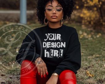 Op de afbeelding: Een zwart sweatshirt met de tekst "YOUR DESIGN HERE" in wit. Het sweatshirt wordt gemodelleerd door een persoon die een rode broek en een zwarte bril draagt.