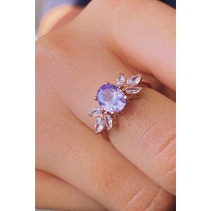 May include: A rose gold ring featuring a large oval purple gemstone surrounded by smaller clear gemstones. The ring is set with a floral design.