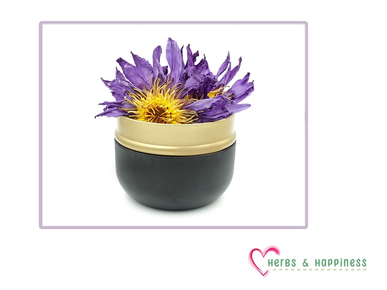 Puede incluir: Un recipiente negro y dorado lleno de una flor morada seca con un centro amarillo. El recipiente tiene una base negra y un borde dorado. La imagen est&aacute; sobre un fondo blanco. El logotipo de Herbs & Happiness est&aacute; en la esquina inferior derecha.