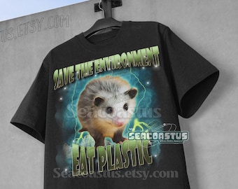 Pode incluir: Camiseta preta com um gráfico de um gambá com o texto "Save the Environment Eat Plastic" em verde e branco.