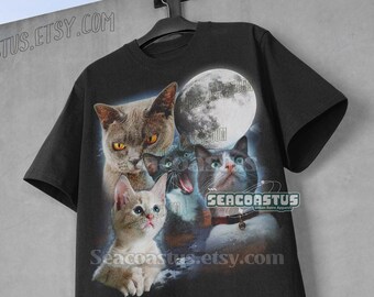 Pode incluir: Camiseta preta com uma estampa gráfica de quatro gatos em frente a uma lua cheia. Os gatos estão olhando para o espectador. O texto "Seacoastus" está impresso na camiseta.